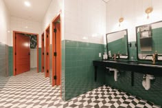 a bathroom with green and white tiles on the floor, two sinks and three mirrors