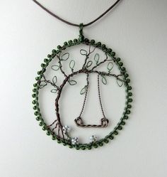 a necklace made out of beads and wire with a tree on the front, hanging from a leather cord