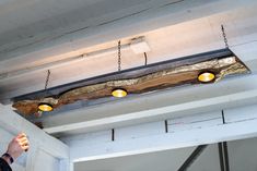 a man standing next to a wooden beam with lights on it's sides and an unfinished piece of wood hanging from the ceiling