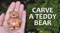 a hand holding a small wooden bear in it's right hand with the words carved a teddy bear on it