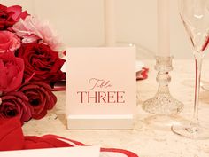 the table is set with red roses and wine glasses, napkins and place cards