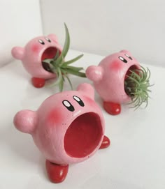 three pink plastic toys with faces on them and one has grass growing out of its mouth