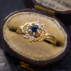 a gold ring with an oval blue stone surrounded by small white diamonds in a velvet case