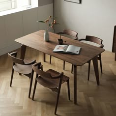 a wooden table with four chairs and a book on top of it in front of a window