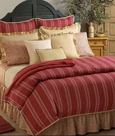 a bed with red and gold comforters in a bedroom next to a dresser, mirror and potted plant