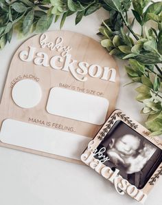 a baby announcement card with a photo frame next to it and greenery on the table