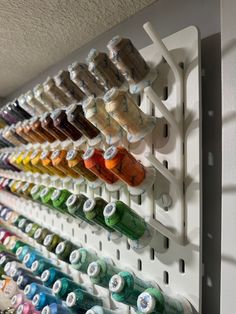 the wall is filled with many different colored spools of thread on it's hooks