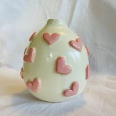 a white vase with pink hearts on it sitting on top of a cloth covered table