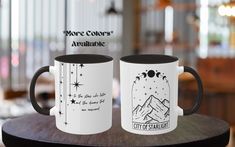 two white and black coffee mugs sitting on top of a wooden table next to each other