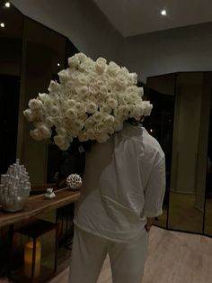 a man holding a bouquet of white roses on his head in front of a mirror