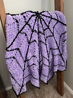 a purple and black crocheted blanket sitting on top of a wooden chair