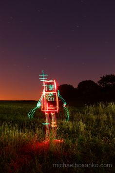 a neon robot standing in the middle of a field at night with stars above it