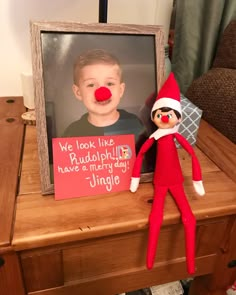 an elf with a red nose sitting next to a picture frame