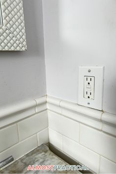 an electrical outlet in the corner of a white tiled bathroom with marble counter tops and floor