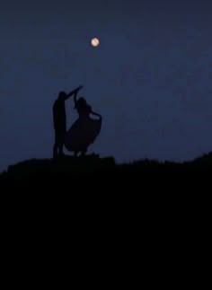 two people are standing on top of a hill at night with the moon in the background