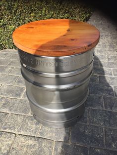 a metal barrel with a wooden top sitting on a brick walkway next to shrubbery