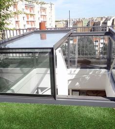 a small glass house sitting on top of a lush green field next to tall buildings