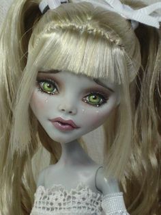 a close up of a doll with blonde hair and green eyes wearing a white dress