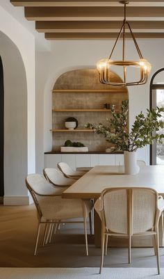 a dining room table with chairs and a potted plant in the center is surrounded by arched doorways