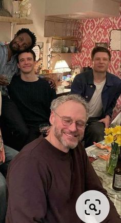 a group of people sitting around a table with wine bottles and flowers in front of them