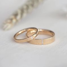 two gold wedding rings sitting next to each other on a white surface with a feather in the background