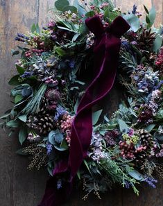 a wreath with purple and green flowers, greenery and berries on it is hung on a wooden surface