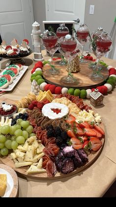 an assortment of cheeses, fruit and crackers on a table with wine glasses