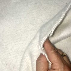 a person's hand is holding the edge of a white blanket that has been pulled back