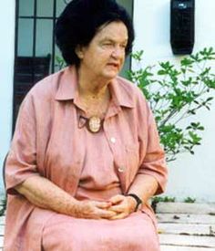 an older woman sitting on a wooden bench in front of a white wall and door