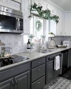 a kitchen with white cabinets and gray counter tops, decorated with greenery on the window sill