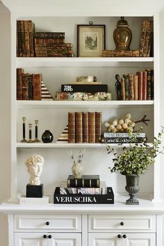 a bookshelf filled with lots of books next to a vase and busturine