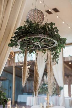 a chandelier with feathers and greenery hanging from it's centerpiece