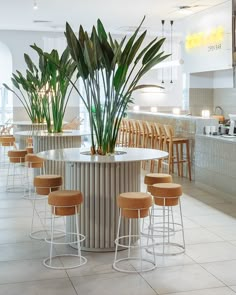 an indoor bar with stools and plants in the center, surrounded by tables and chairs