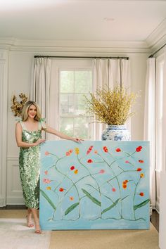 a woman standing next to a large painting in a living room with flowers on it