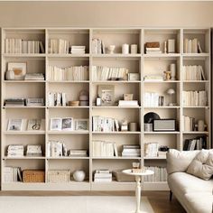 a living room filled with lots of white furniture and bookshelves full of books