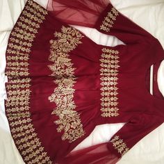 a red dress with gold embroidered details on the neckline and sleeves, sitting on a bed