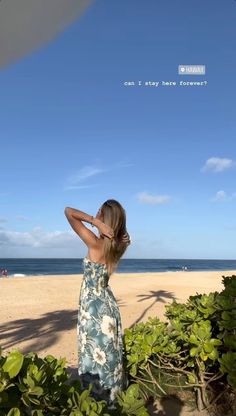 a woman standing on top of a sandy beach next to the ocean with her arms behind her head