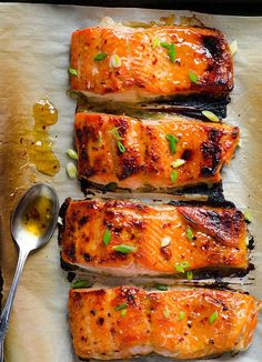 four pieces of cooked salmon sitting on top of a piece of parchment paper next to a spoon