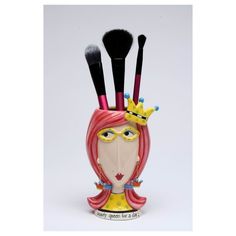 a cup with makeup brushes in it and a face painted on the side, as well as a crown