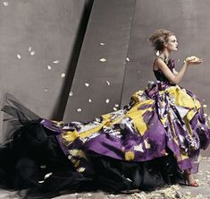 a woman in a purple and yellow dress with petals falling from her hands on the ground