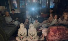 a group of people sitting in a living room with ghost dolls on the couches