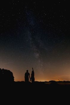 two people standing on top of a hill under the night sky