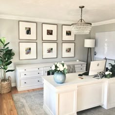 a home office with white furniture and pictures on the wall above it, along with potted plants