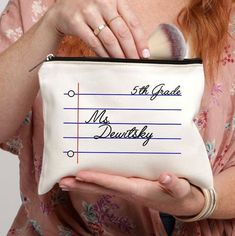 a woman holding a makeup bag with writing on it