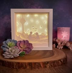 an illuminated nativity scene with flowers on a wooden table next to a lit candle