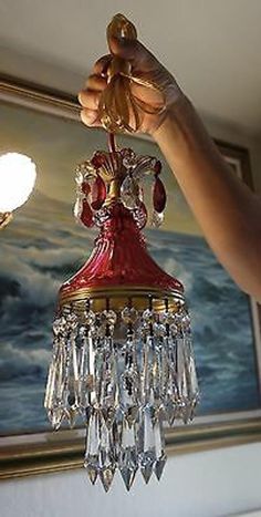 a person holding up a red and gold chandelier in front of a painting