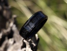 a wedding band with black speckles sits on top of a piece of wood