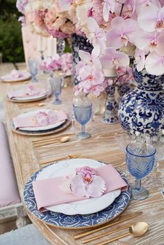 the table is set with blue and white plates, pink napkins, and flowers