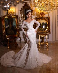 a woman in a white wedding dress standing next to a mirror and chandelier