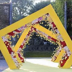 a yellow frame with flowers on it in the middle of a park area that has trees and bushes behind it